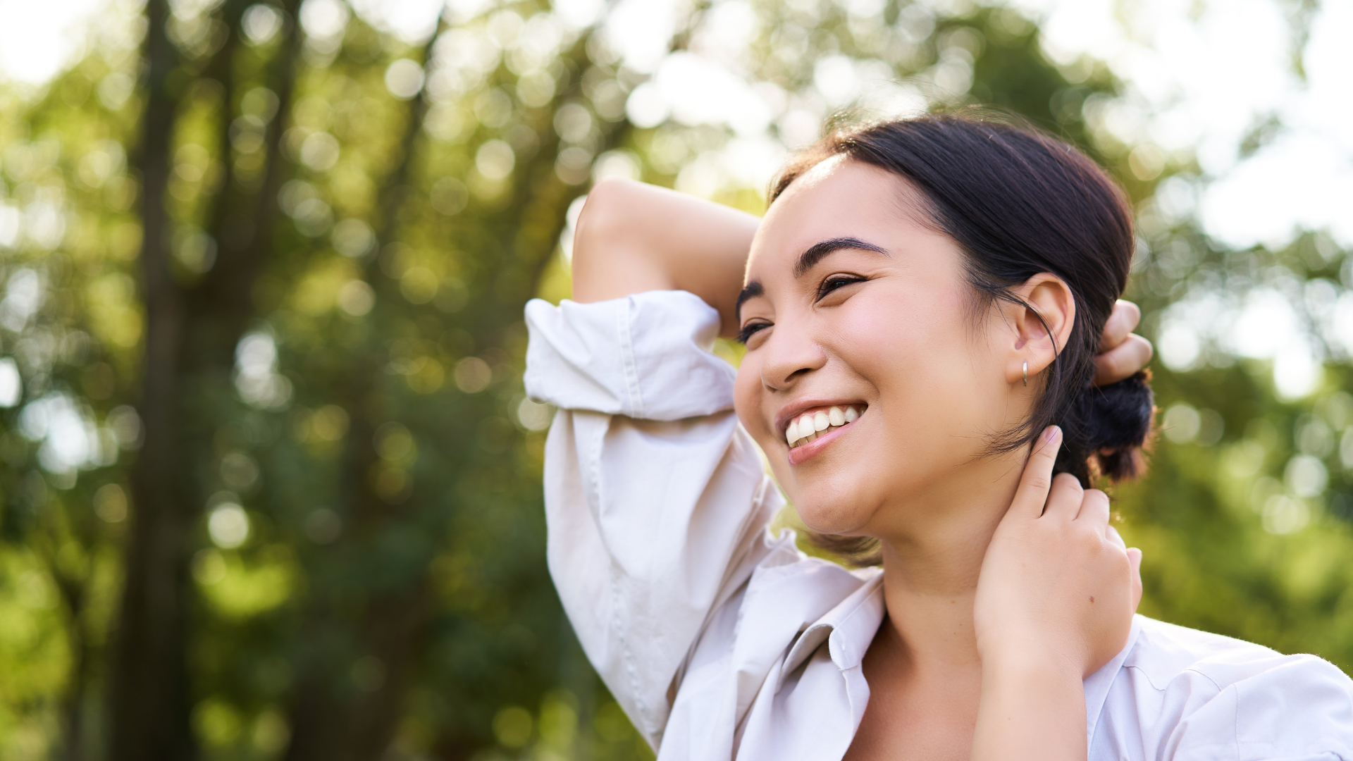 Smiling person in a white shirt outdoors with trees in background.