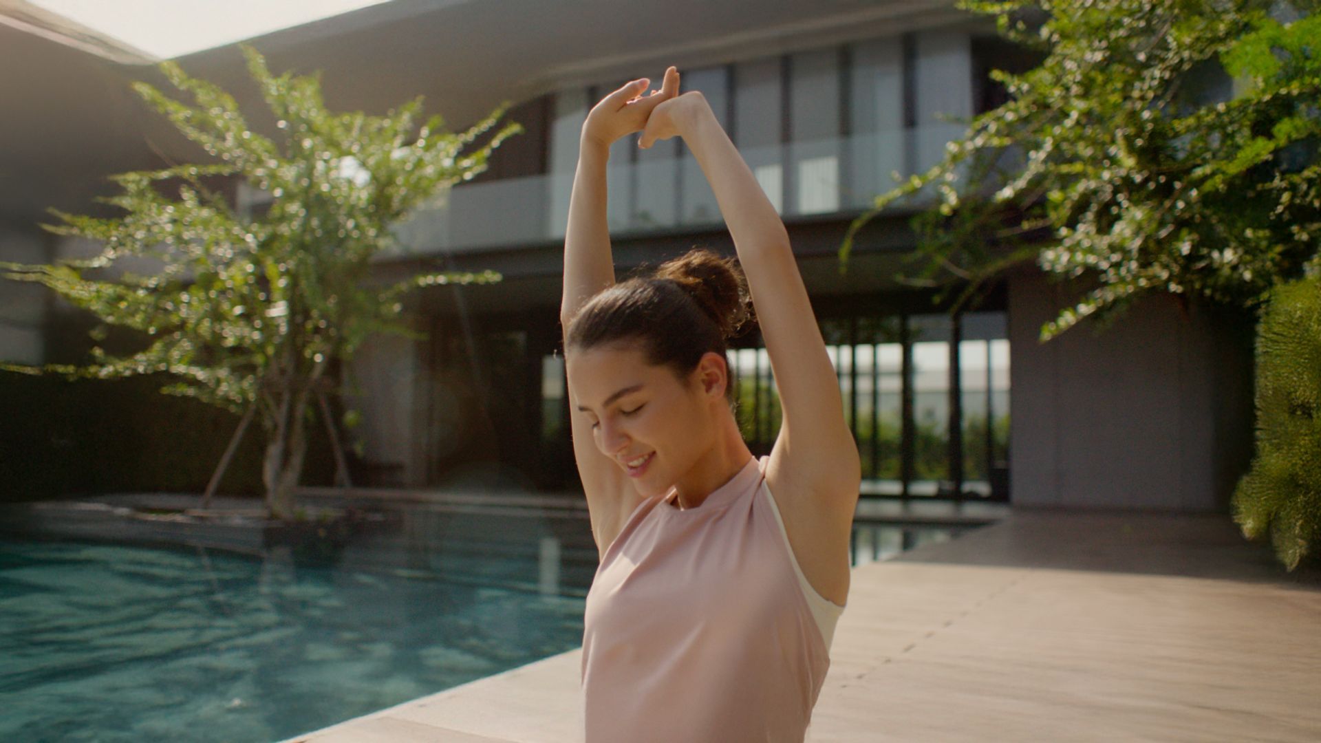 Woman stretching by a pool in sunlight.