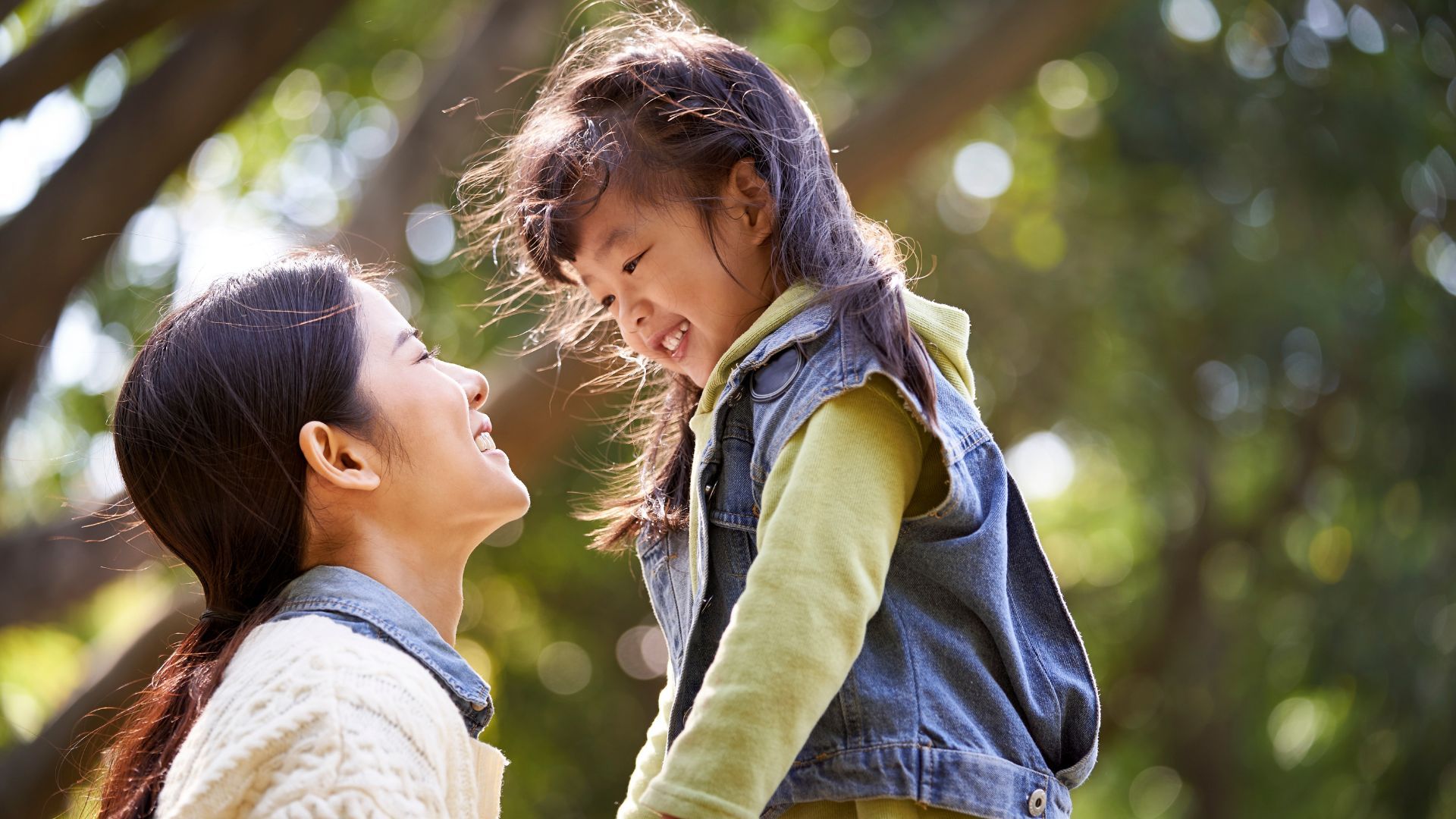 Smiling woman and child outdoors, looking at each other.
