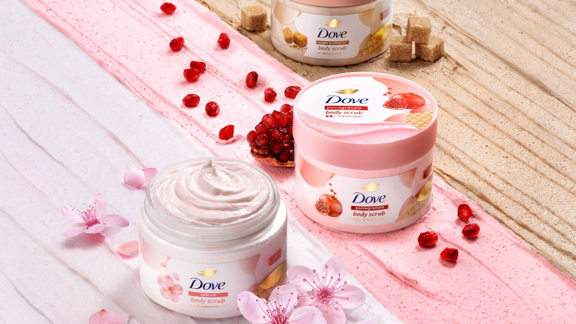 Dove body scrub jars arranged with pink flowers, pomegranate seeds, and sugar cubes.