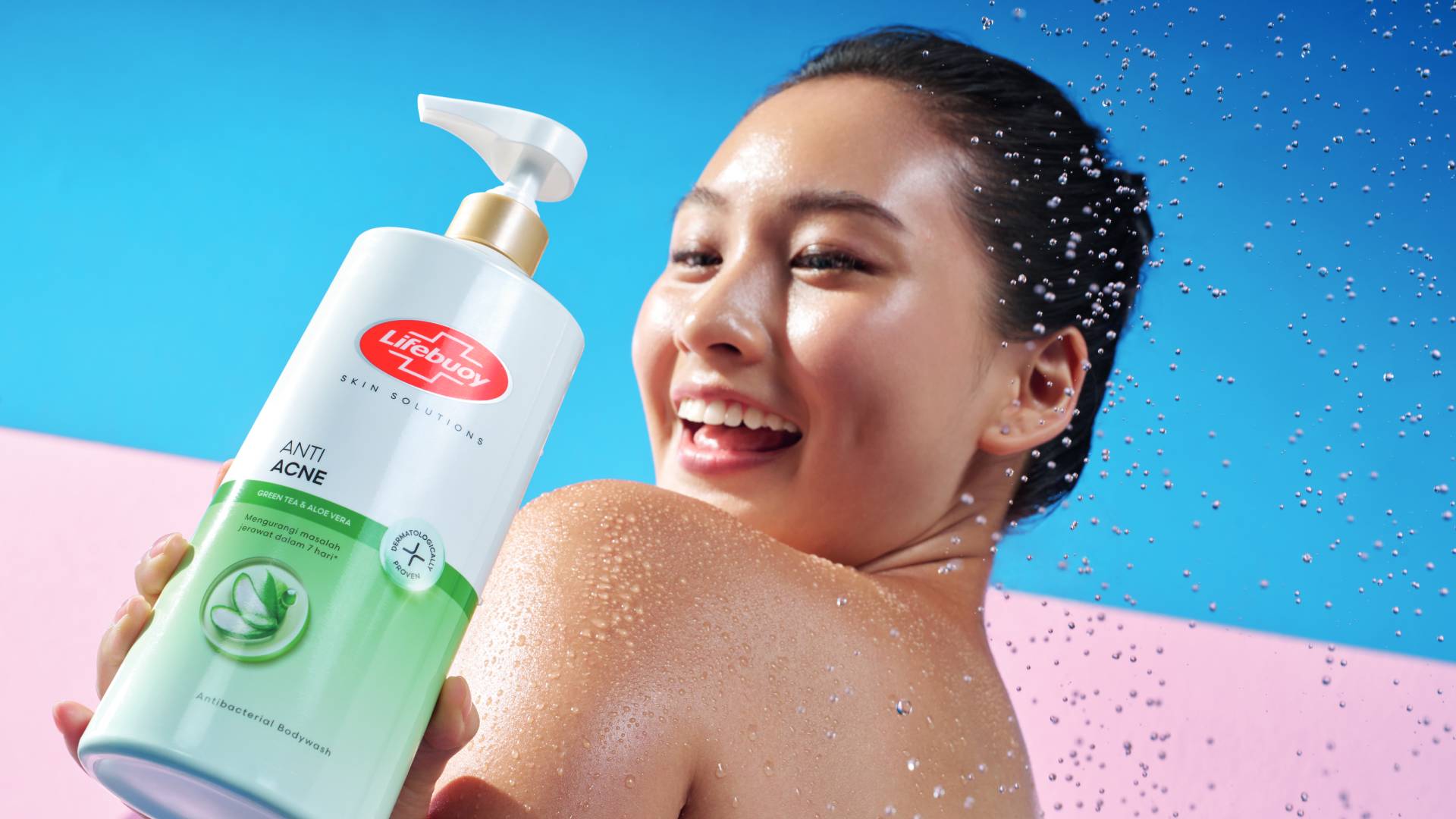 Seorang wanita tersenyum memegang sabun mandi antibakteri Lifebuoy Anti Jerawat -– botol putih dan hijau dengan logo Lifebuoy merah.