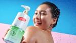 Seorang wanita tersenyum memegang sabun mandi antibakteri Lifebuoy Anti Jerawat -– botol putih dan hijau dengan logo Lifebuoy merah.