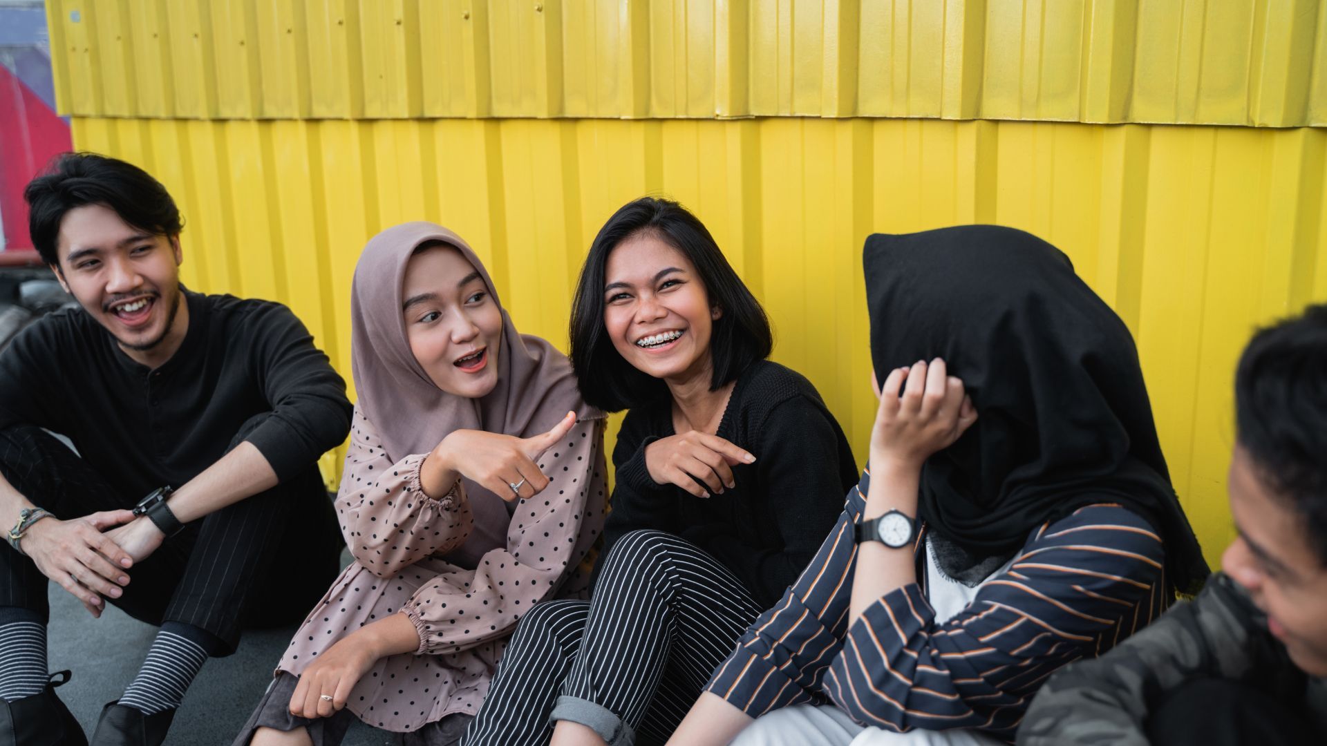 Group of friends laughing against yellow wall.