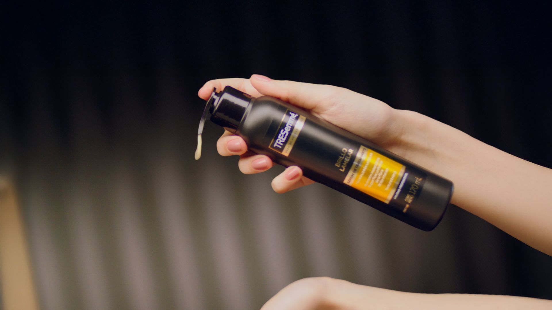 Hand holding TRESemmé bottle, dispensing product.